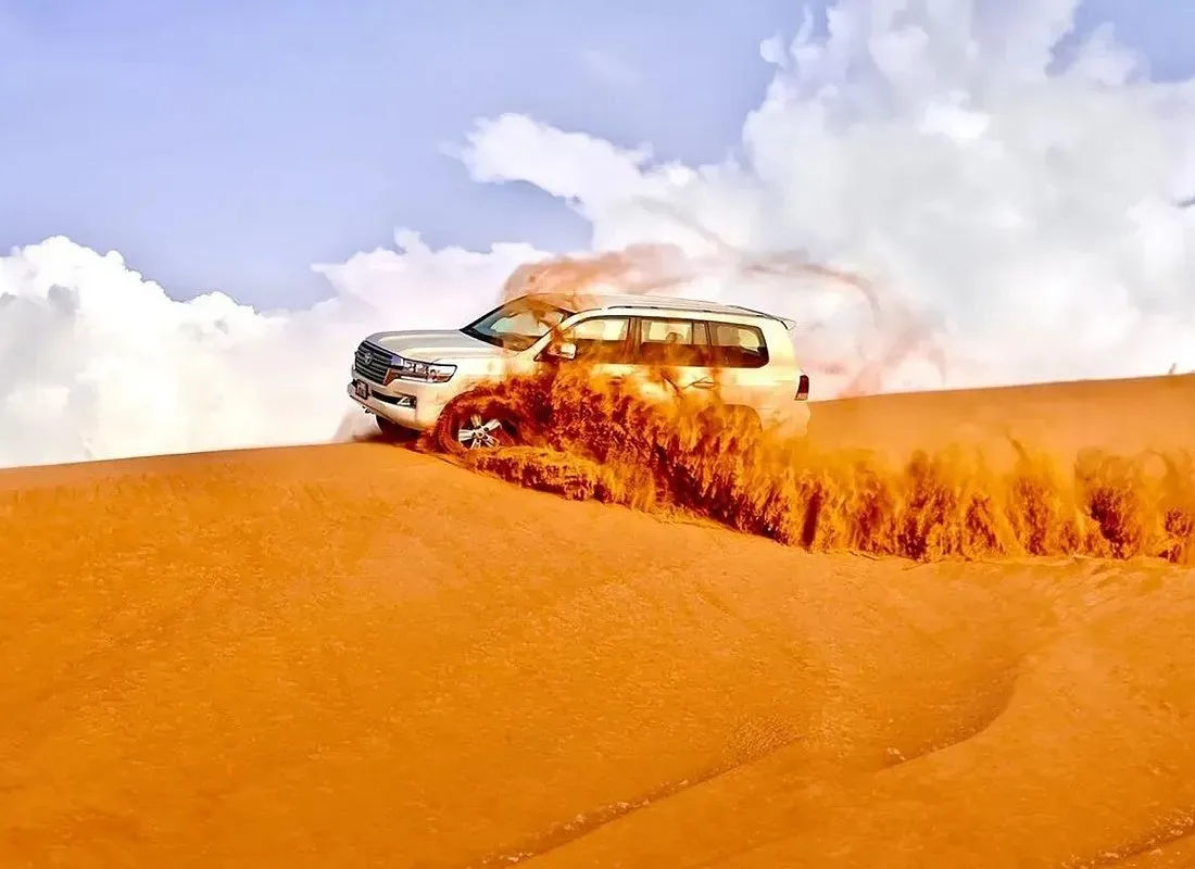 Dune bashing in the Dubai desert A white 4x4 kicking up a dramatic wall of orange sand while dune bashing in the Dubai desert